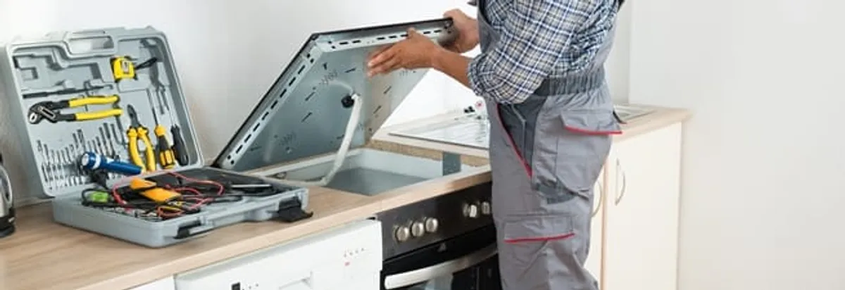 Cooktop repair technician lifting a built-in stovetop for service in Madison, WI