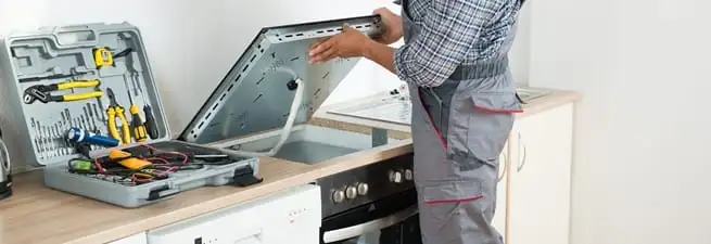 Cooktop repair technician lifting a built-in stovetop for service in Madison, WI