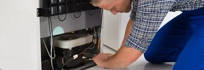 Refrigerator repair technician servicing the compressor and condenser area in Madison, WI