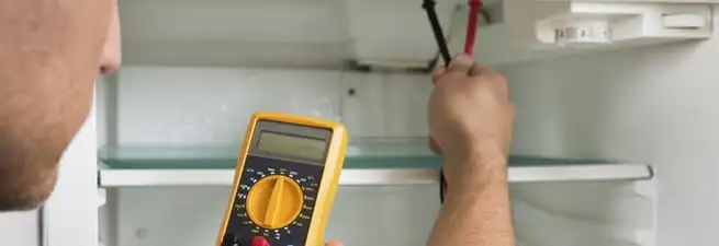 Refrigerator repair technician testing electrical components with a multimeter in Madison, WI